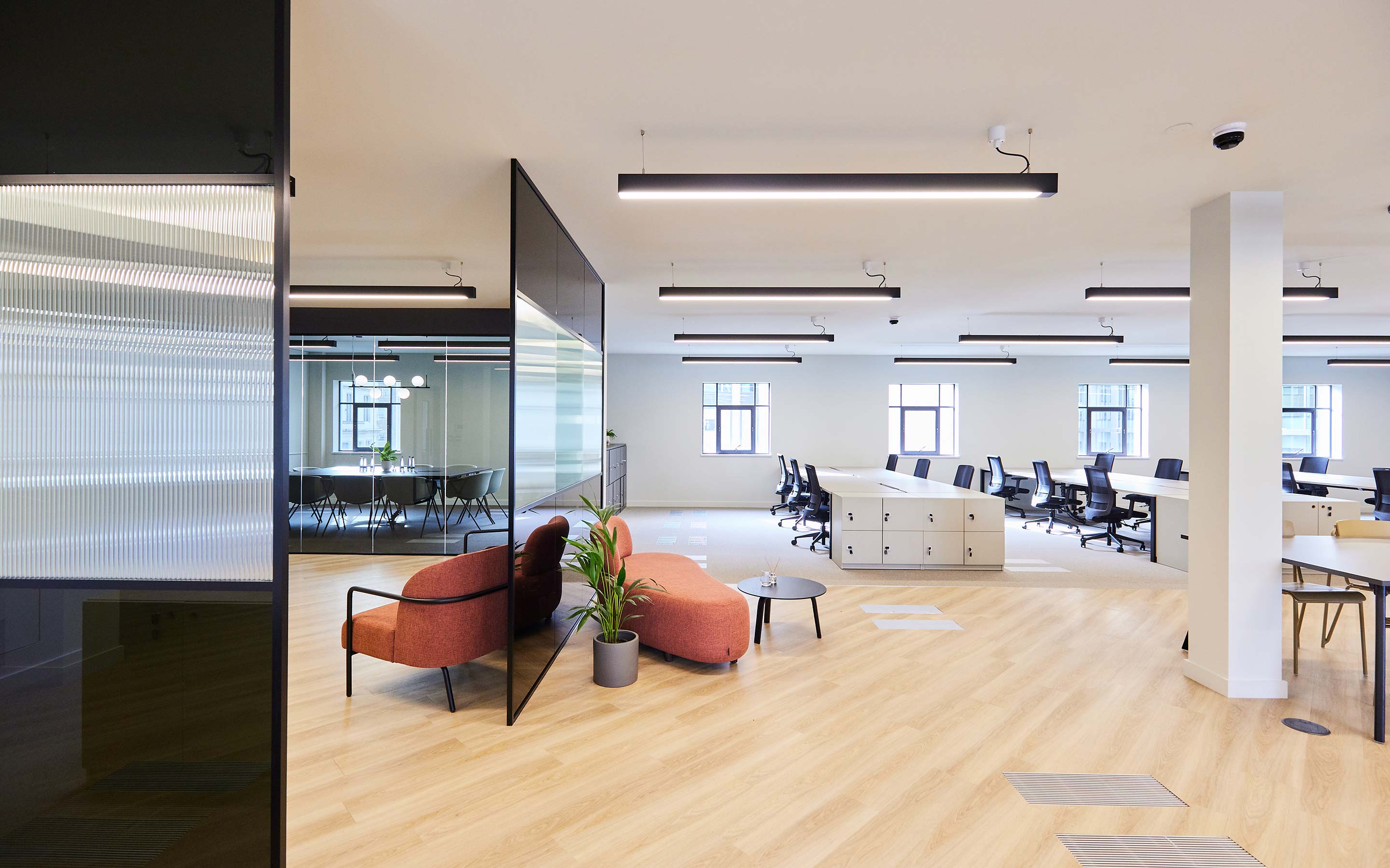 Spacious London office with open-plan desking, pale wooden floors, and soft-seating for visitors to relax
