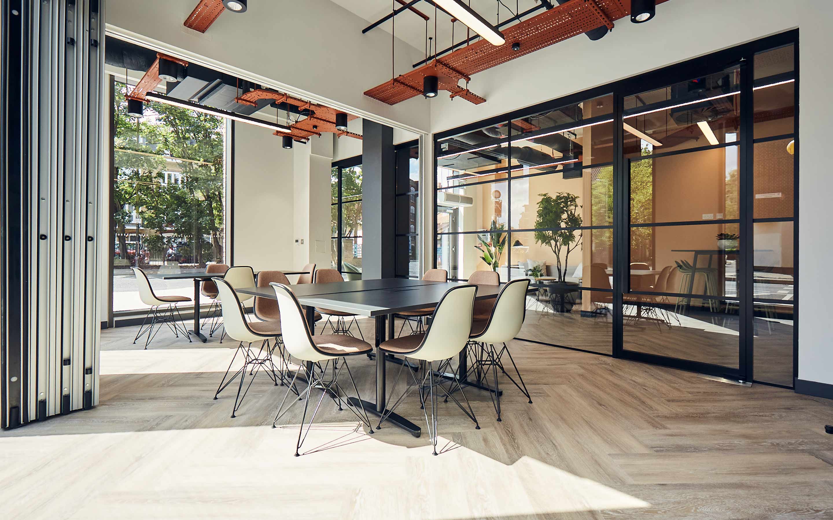 The image shows a sunny office interior, with glass meeting walls and cool tables and chairs