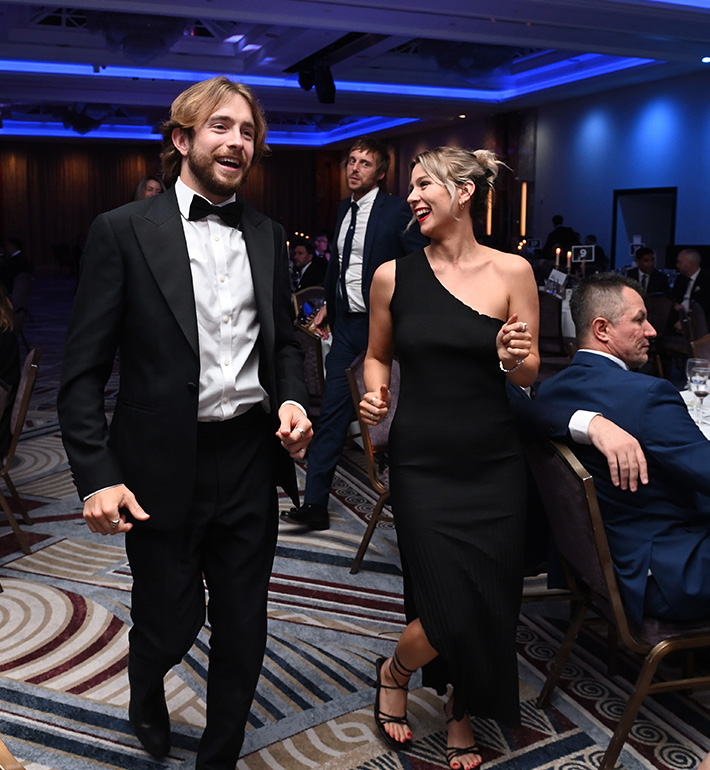 A couple in formal attire at an event with guests seated around them.