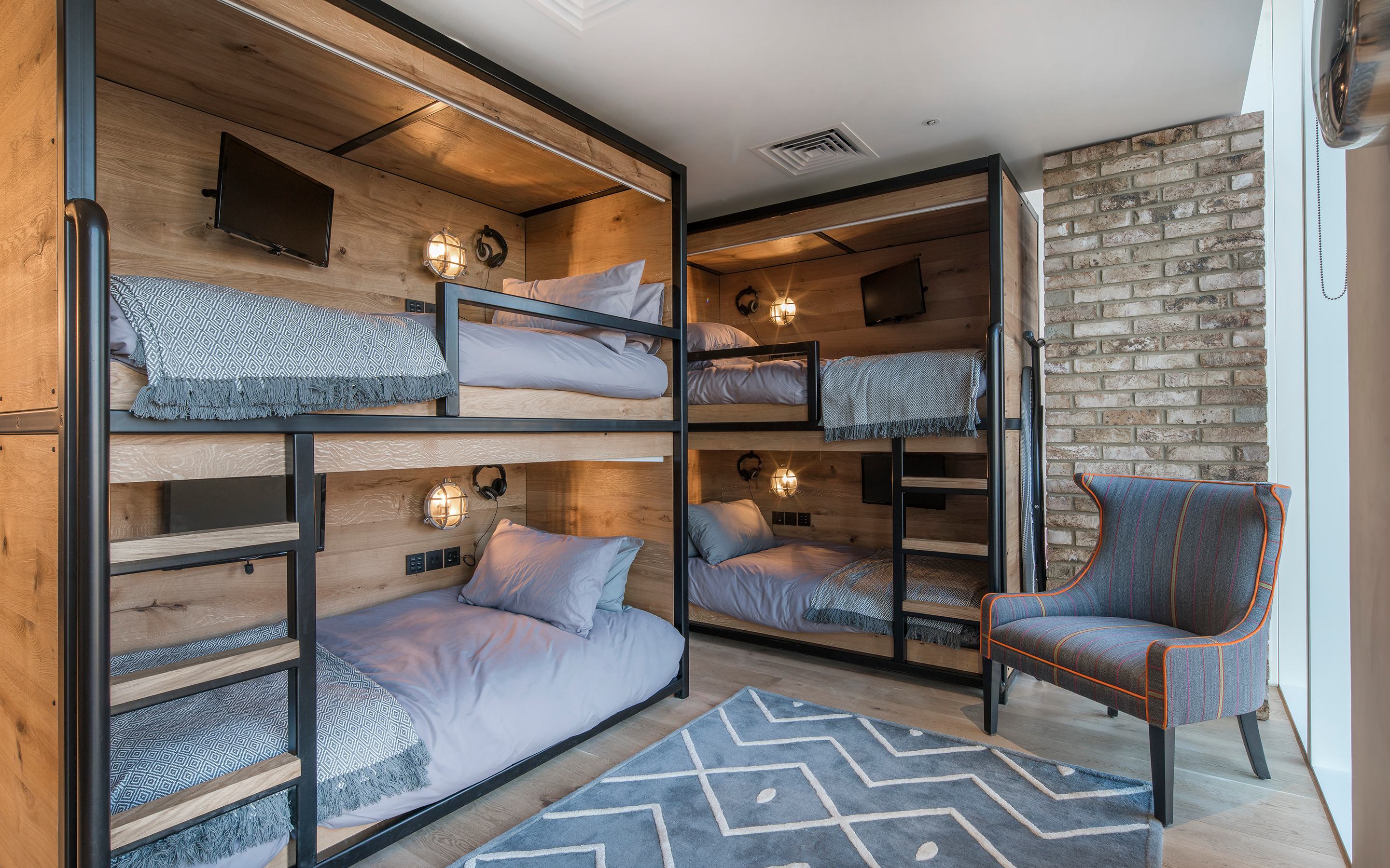 Four bunkbeds with grey bedding and TVs within them, and a grey and orange striped arm chair.