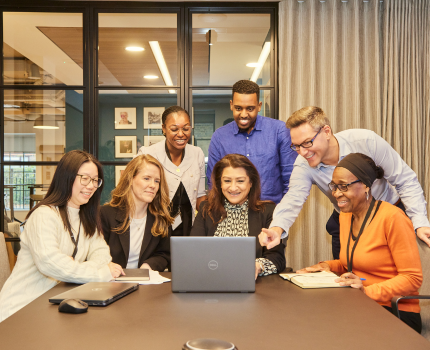 Group of professionals engaged in a meeting around a table with a laptop.