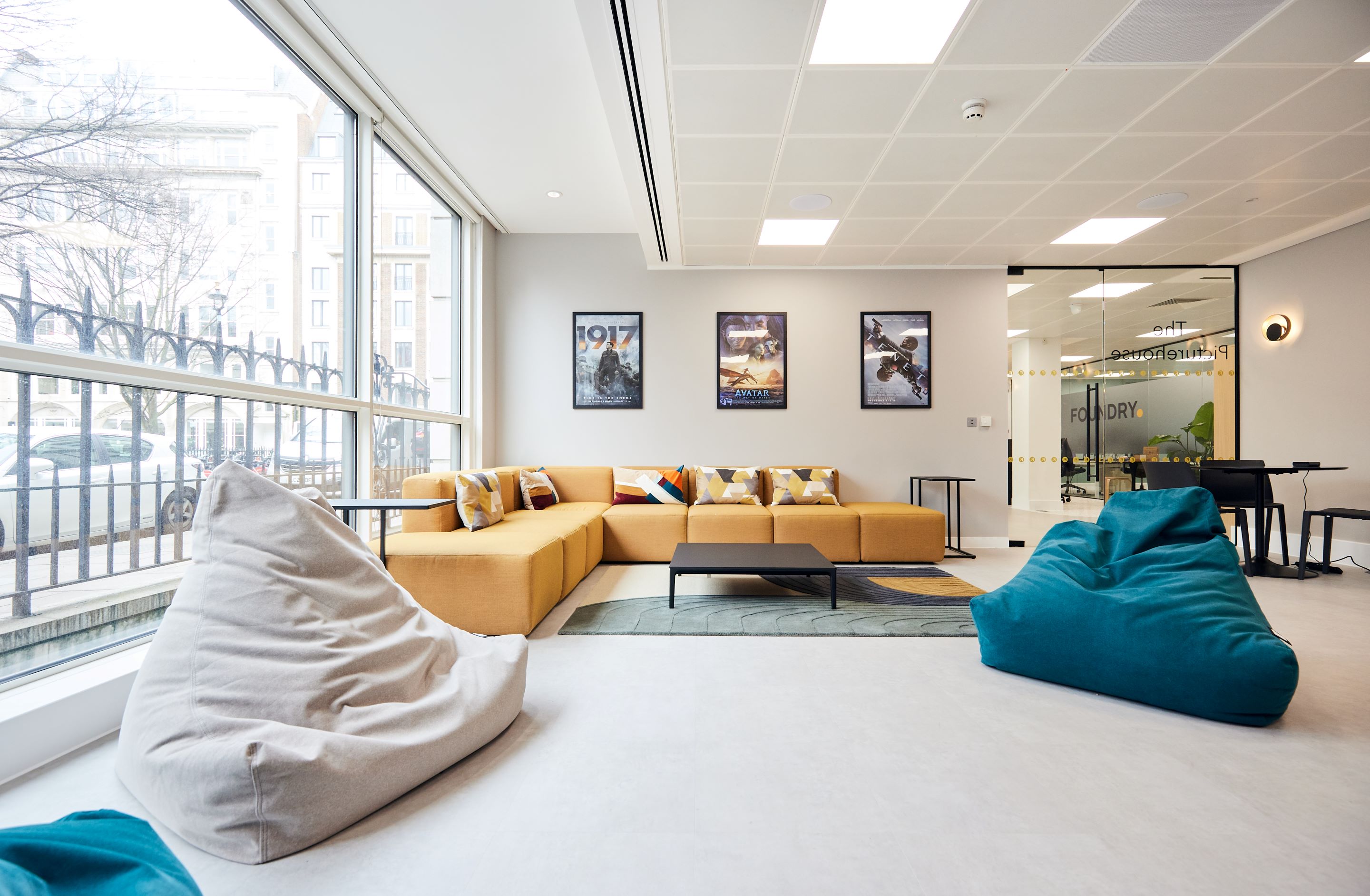 Modern office lounge with a yellow couch, bean bags, movie posters, and large windows.