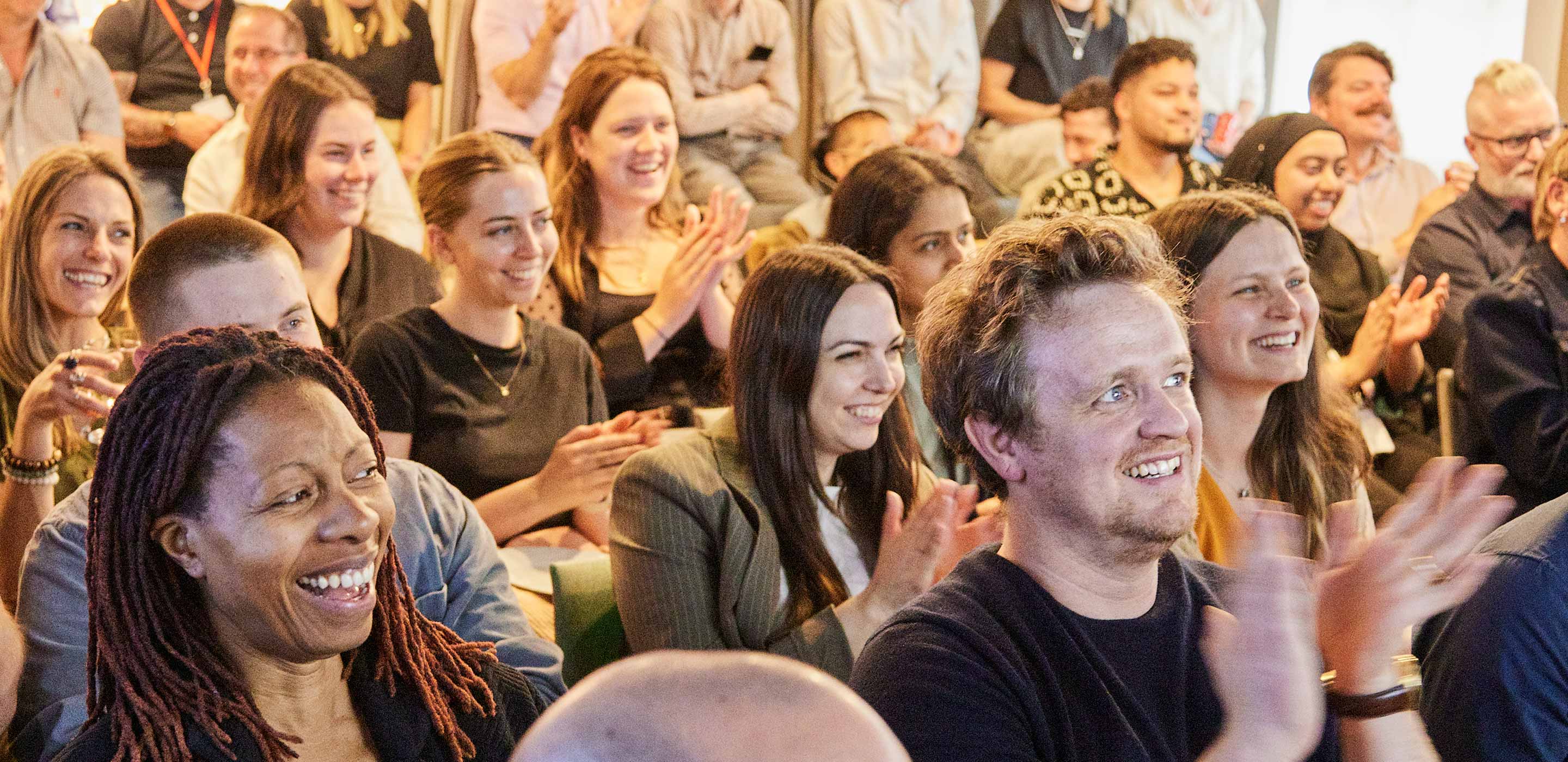 A group of colleagues in an all hands meeting smiling and clapping