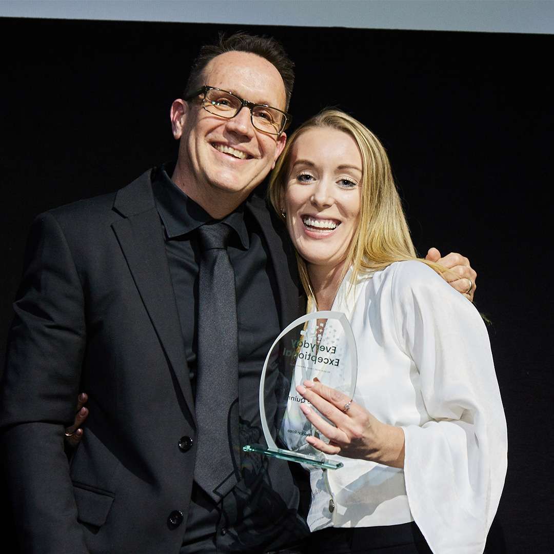 A man and woman proudly stand together, holding an award, showcasing their achievement and teamwork