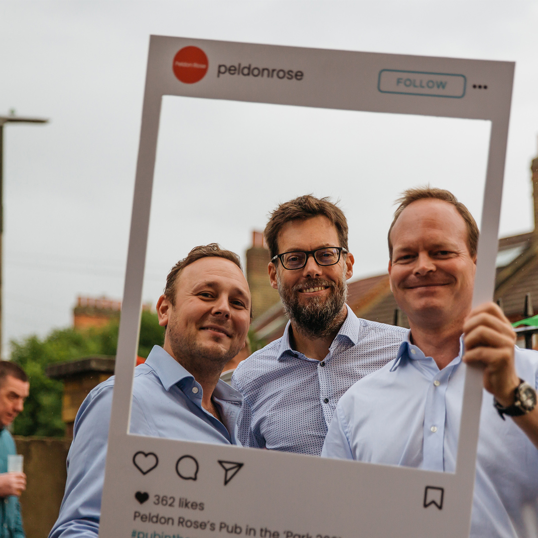 Three men stand together, lifting a picture of themselves, symbolizing their camaraderie