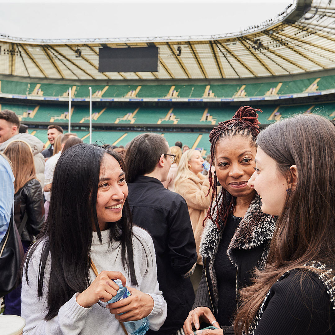 At a stadium, three women converse animatedly, enjoying the event and each other's company amidst the crowd