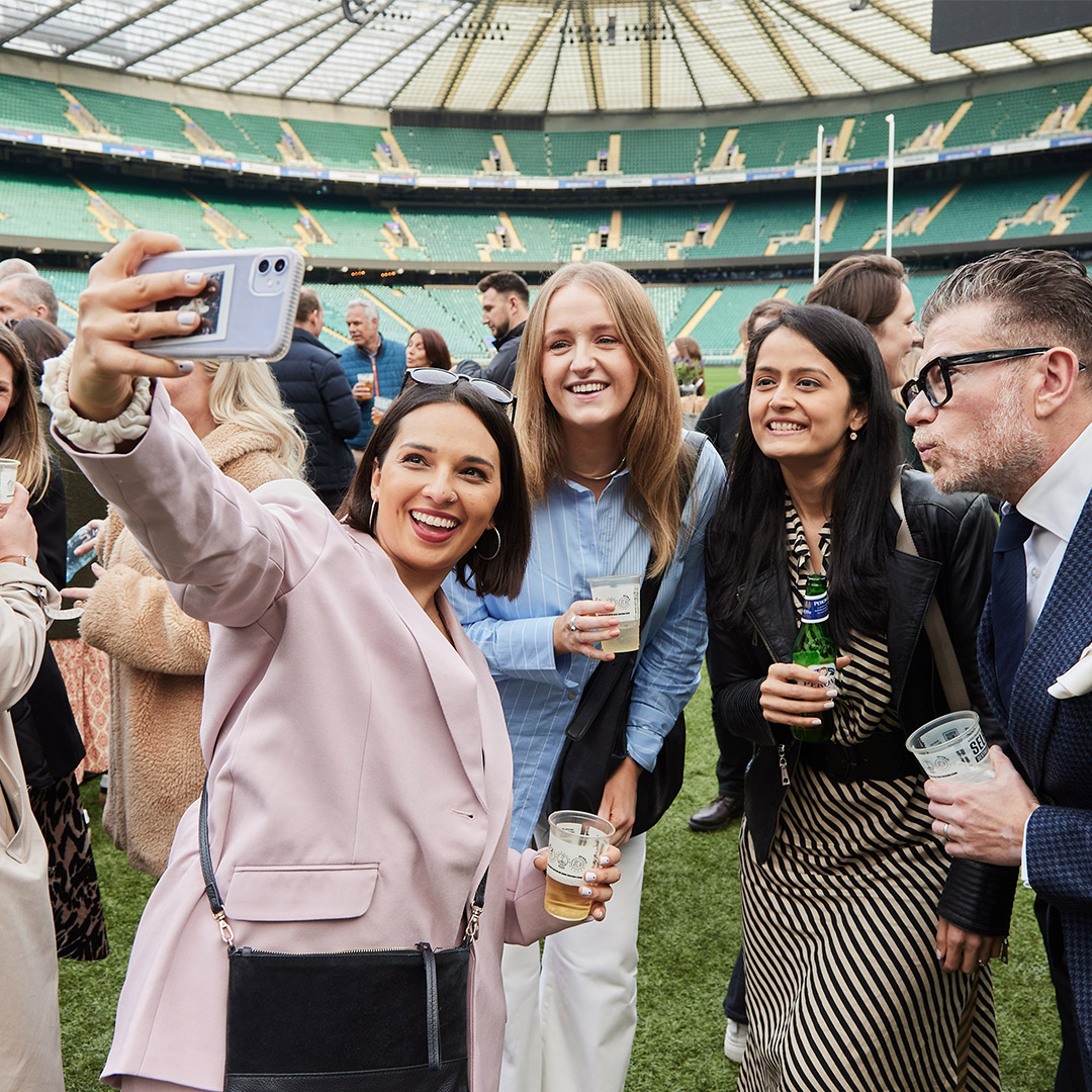 A cheerful group of friends taking a selfie at a rugby stadium showcasing excitement and camaraderie