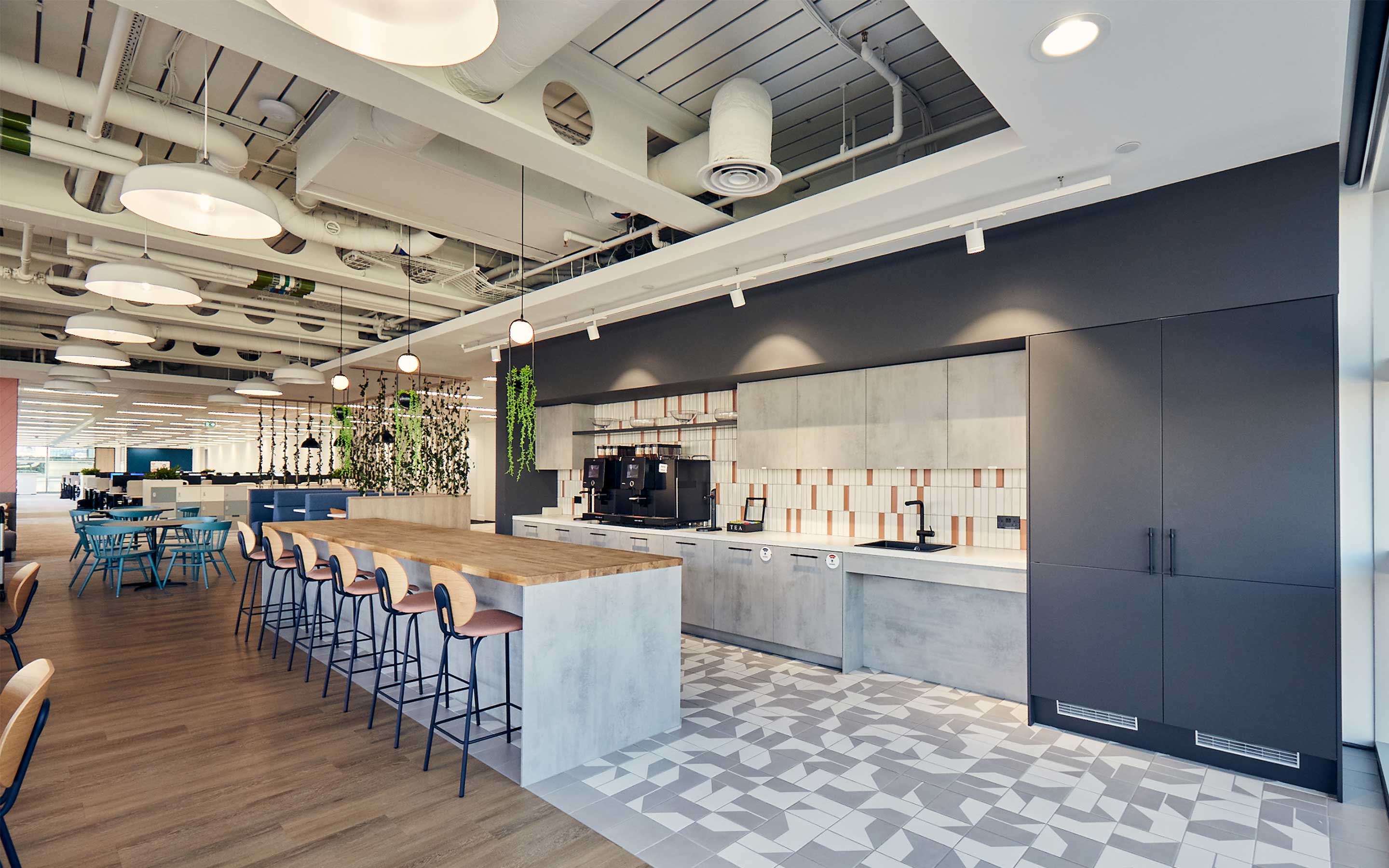 A sleek office teapoint with breakfast bar stools, shiny grey counters and hanging plants