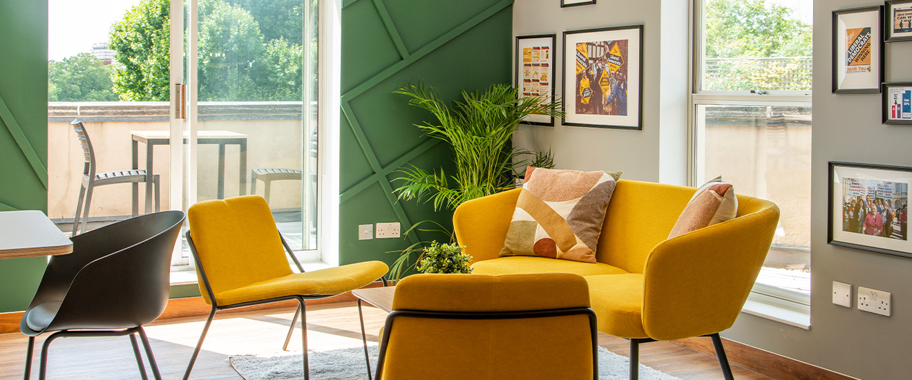 A wellbeing space with a yellow sofa and chairs with sliding glass doors and framed photos on the walls.