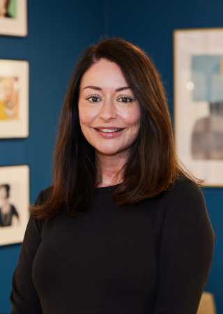 Woman in a black top standing in front of a wall with framed artwork.