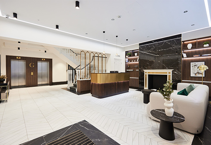 Modern hotel lobby with reception desk, seating area, staircase, and elegant decor.