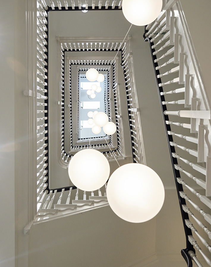 A view looking up a rectangular spiral staircase with spherical light fixtures.