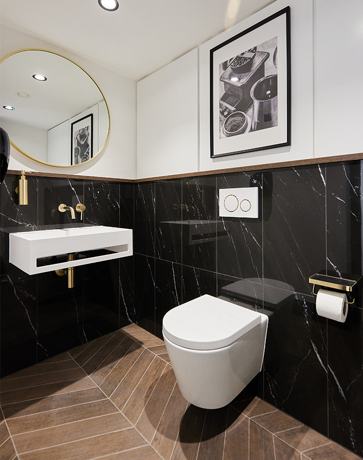 Modern bathroom with black marble walls, gold accents, and framed art above the toilet.