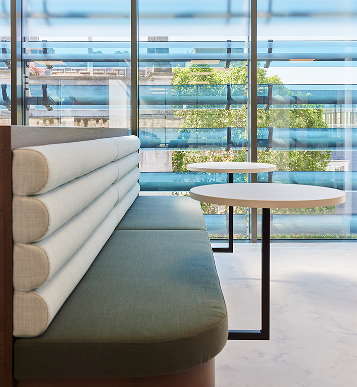 Modern lobby with upholstered bench and round tables near floor-to-ceiling windows.