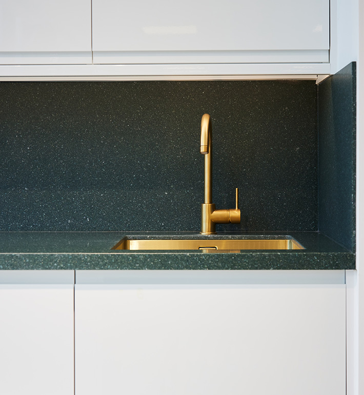 Modern kitchen with gold faucet and undermount sink against dark speckled backsplash.