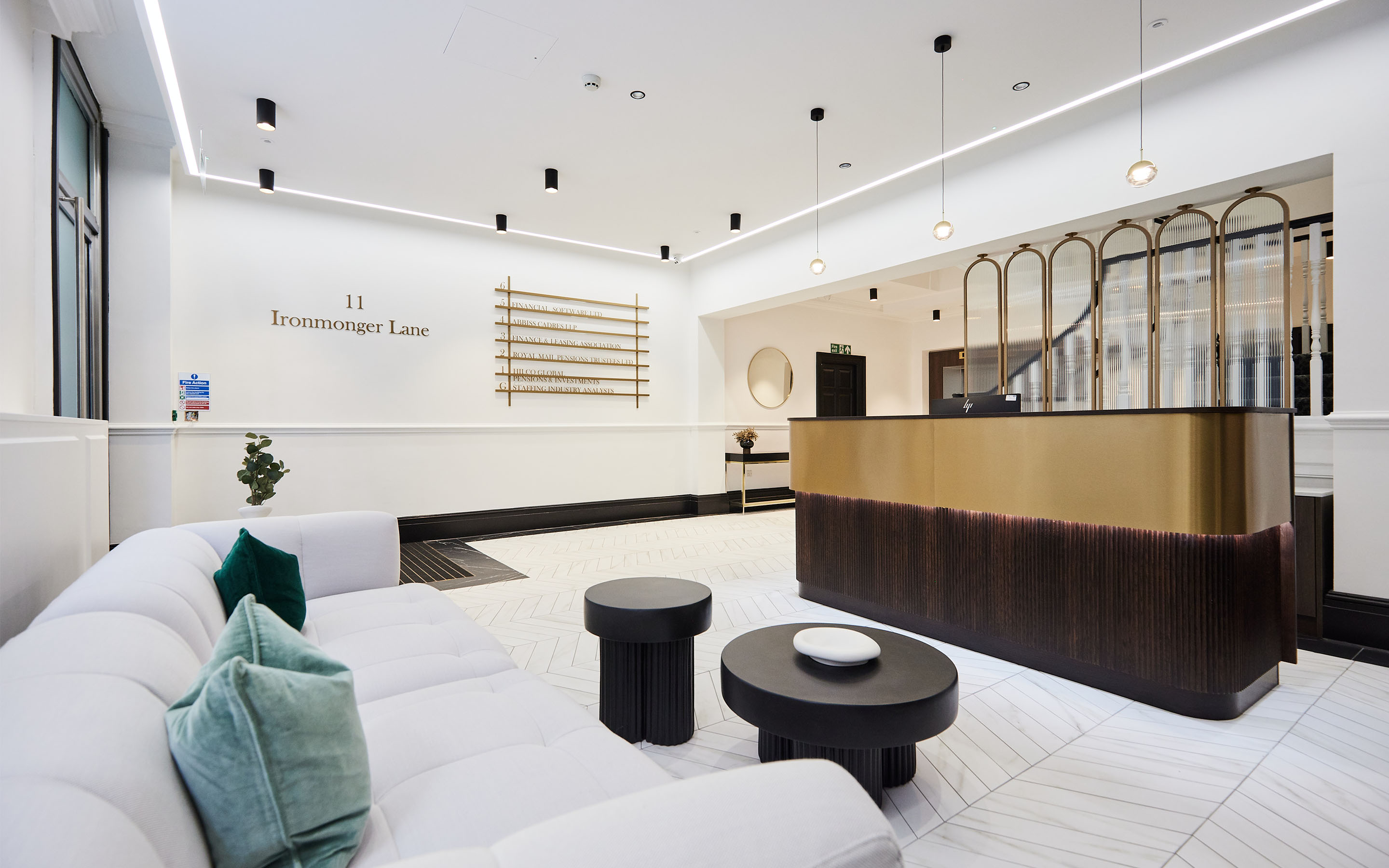 Modern lobby with a white sofa, black tables, a reception desk, and sleek lighting.