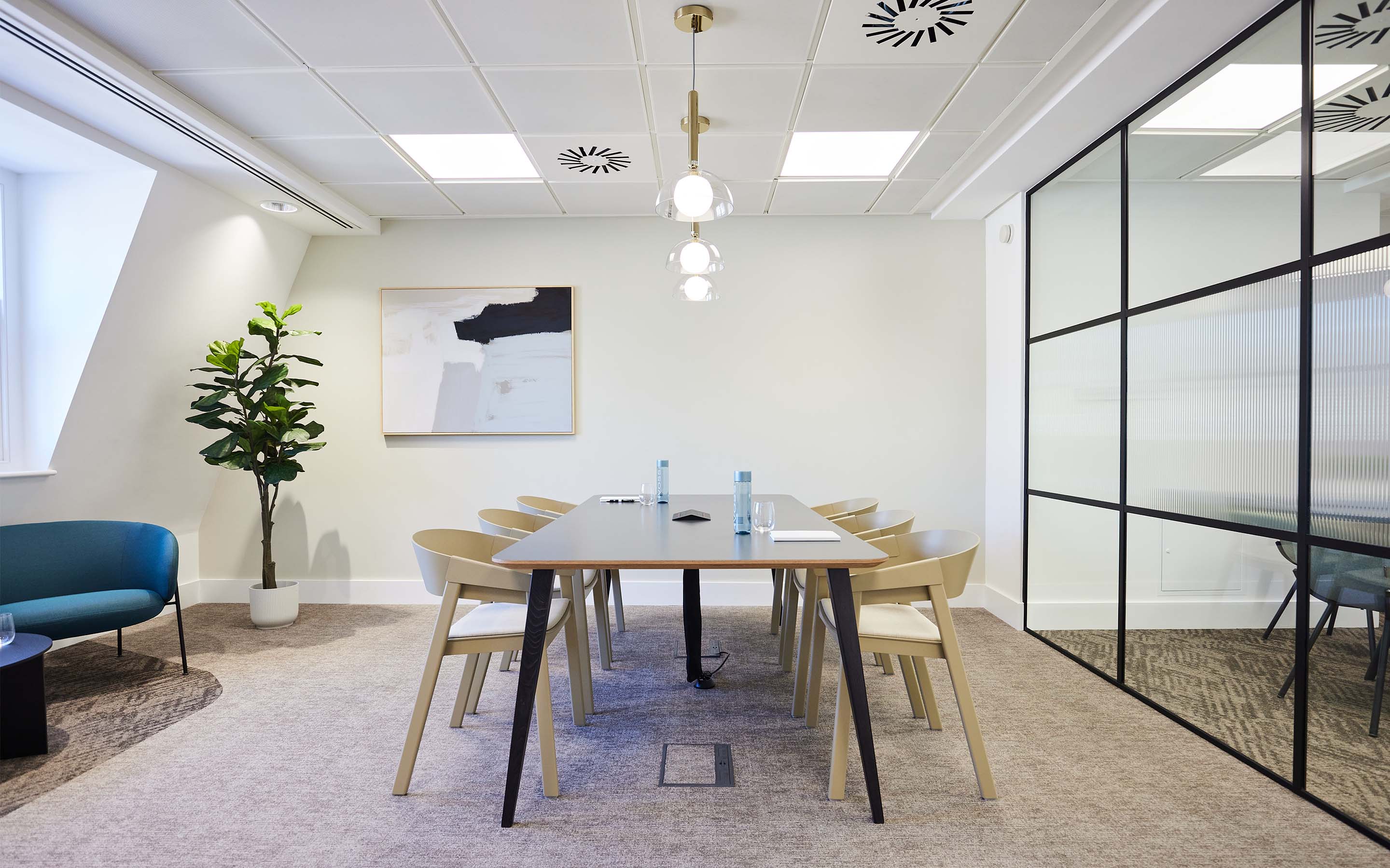 Modern office meeting room with a table, chairs, a potted plant, and abstract art on the wall.