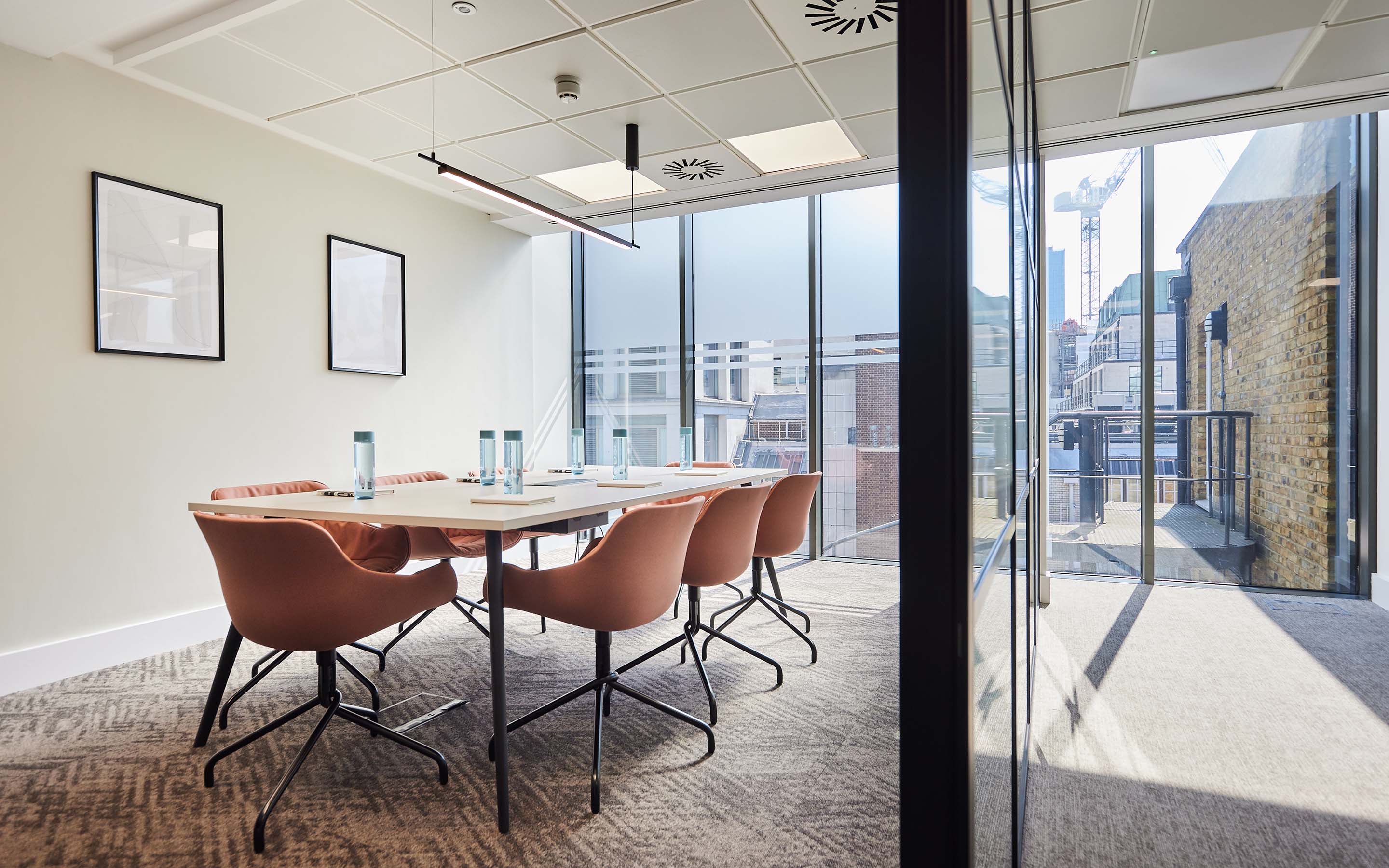 Modern conference room with a long table, tan chairs, framed art on walls, and large windows.