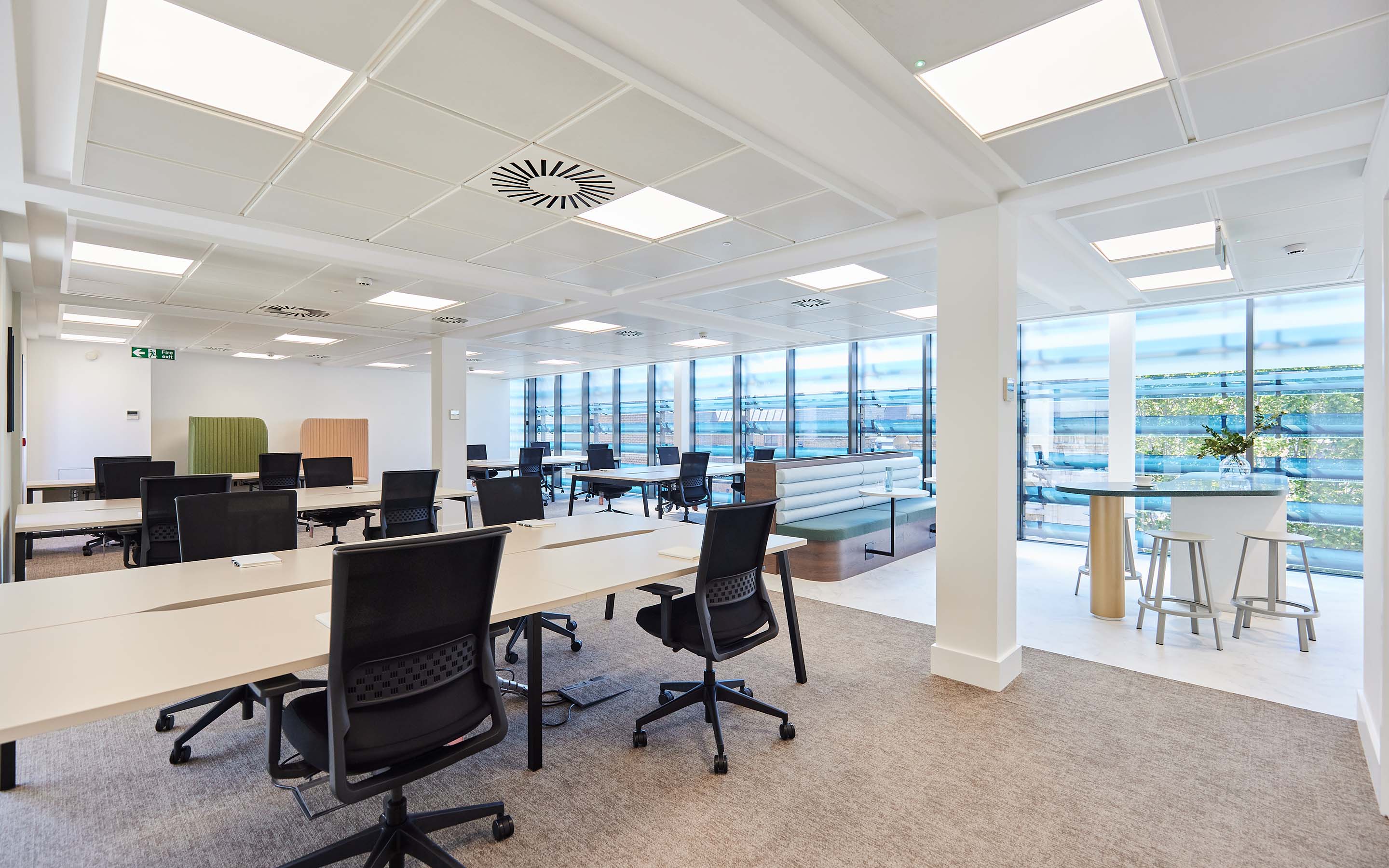 Bright, modern office with desks, chairs, and a lounge area by large windows.