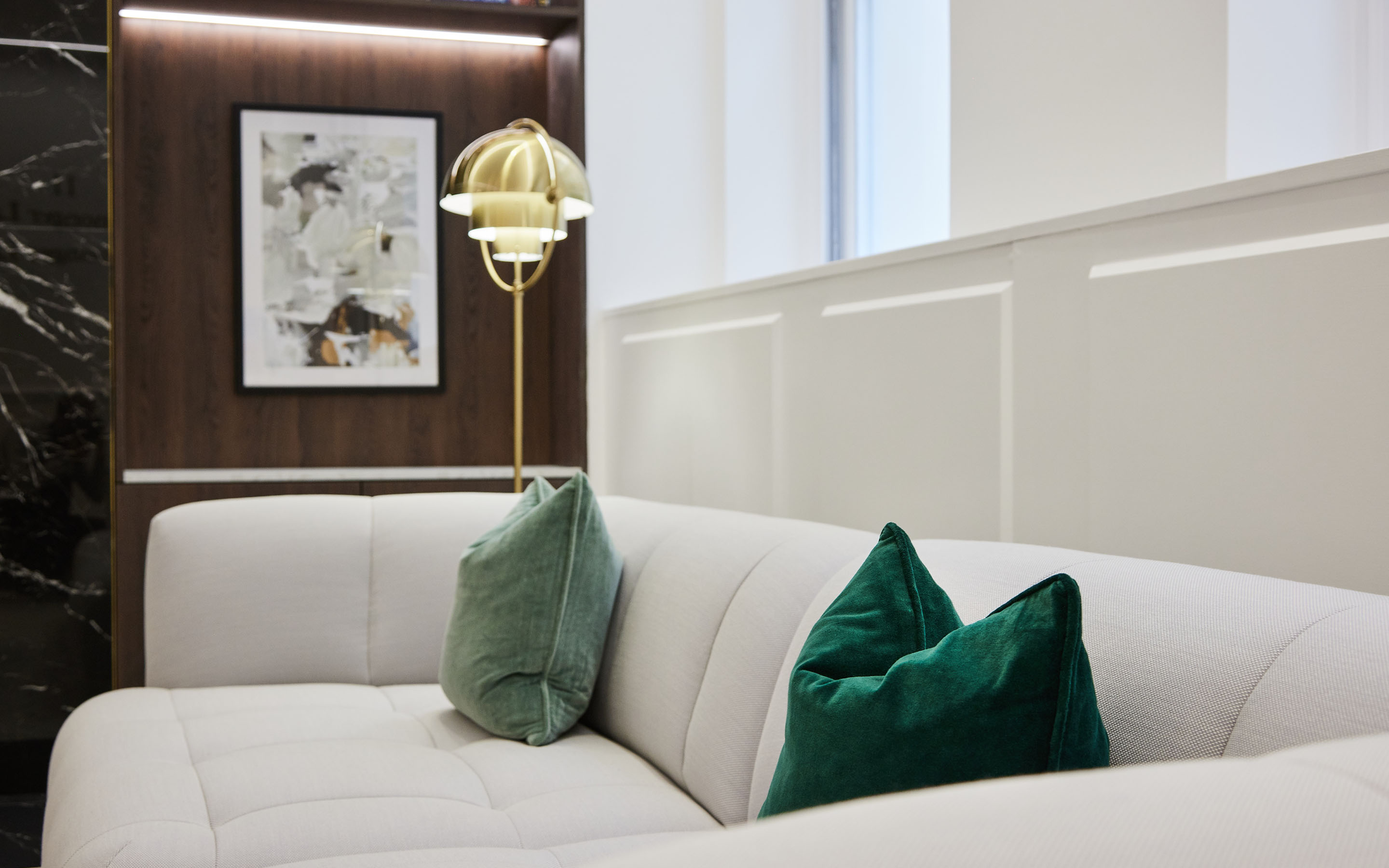 Modern living room with white sofa, green velvet pillows, and a stylish gold lamp.