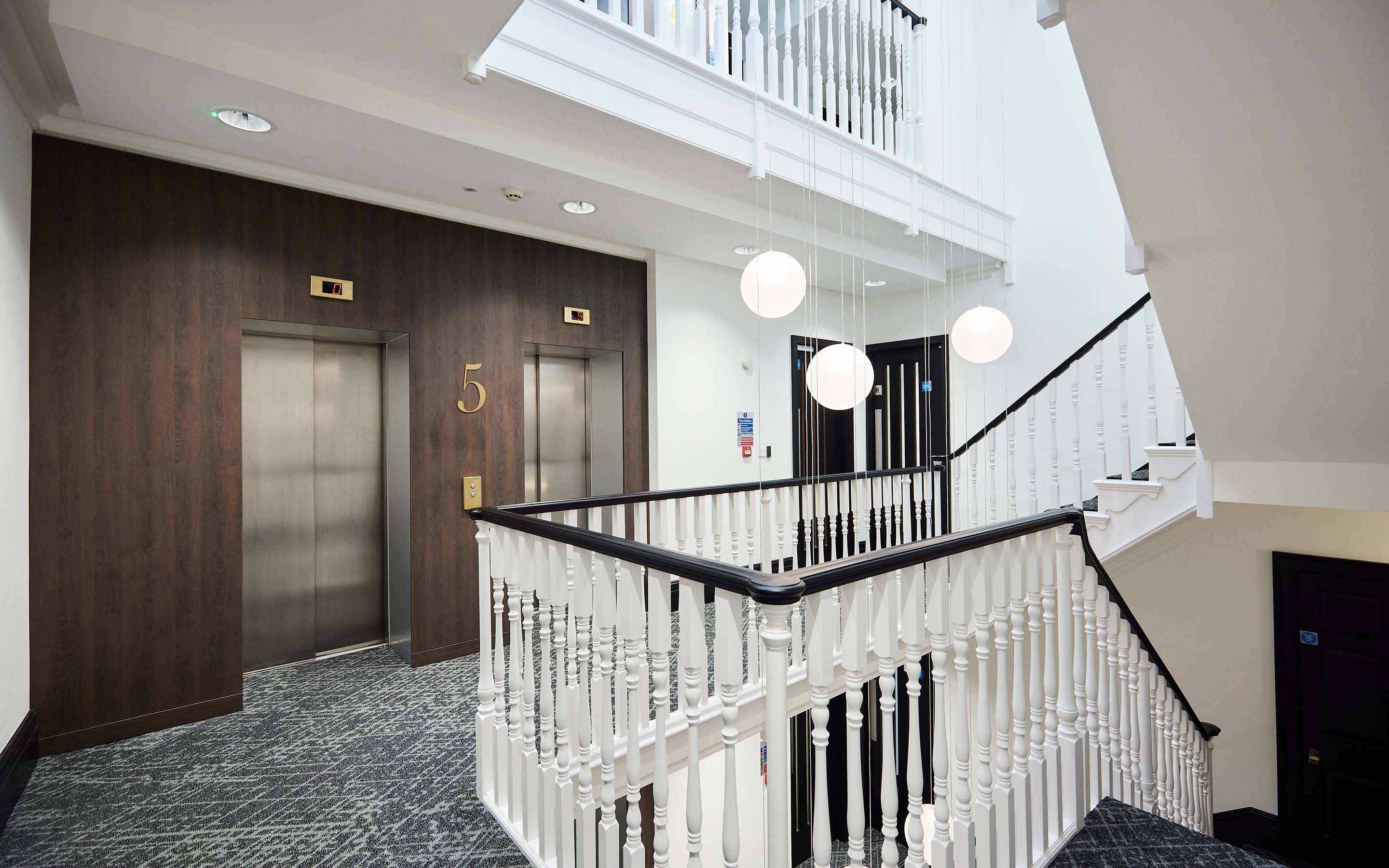 Modern lobby with two elevators, staircase, and hanging spherical lights.