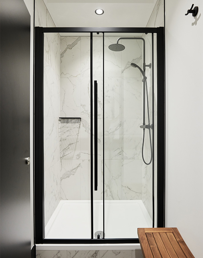 Modern shower with marble walls and black frame doors, plus a wooden bench outside.