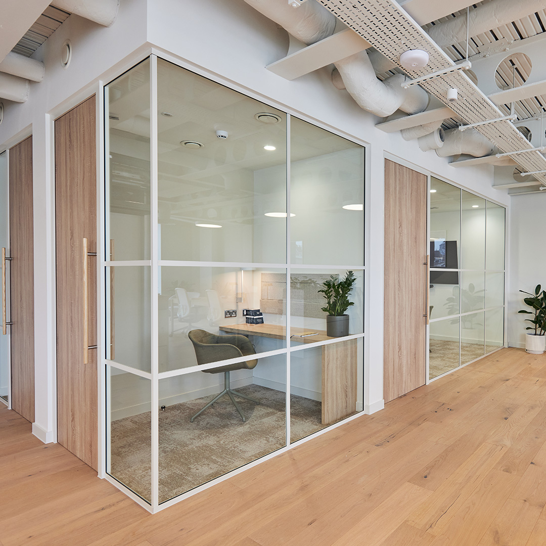 Two glass walled zoom rooms in a contemporary workplace, characterised by a sleek and neutral office interior desking