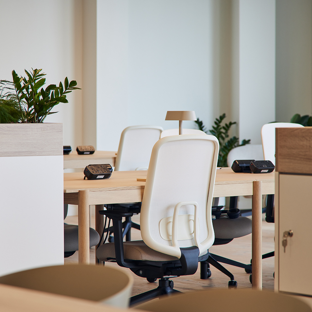 Detail shot of a white office ergonomic desk chair, with desks, AV, and planters