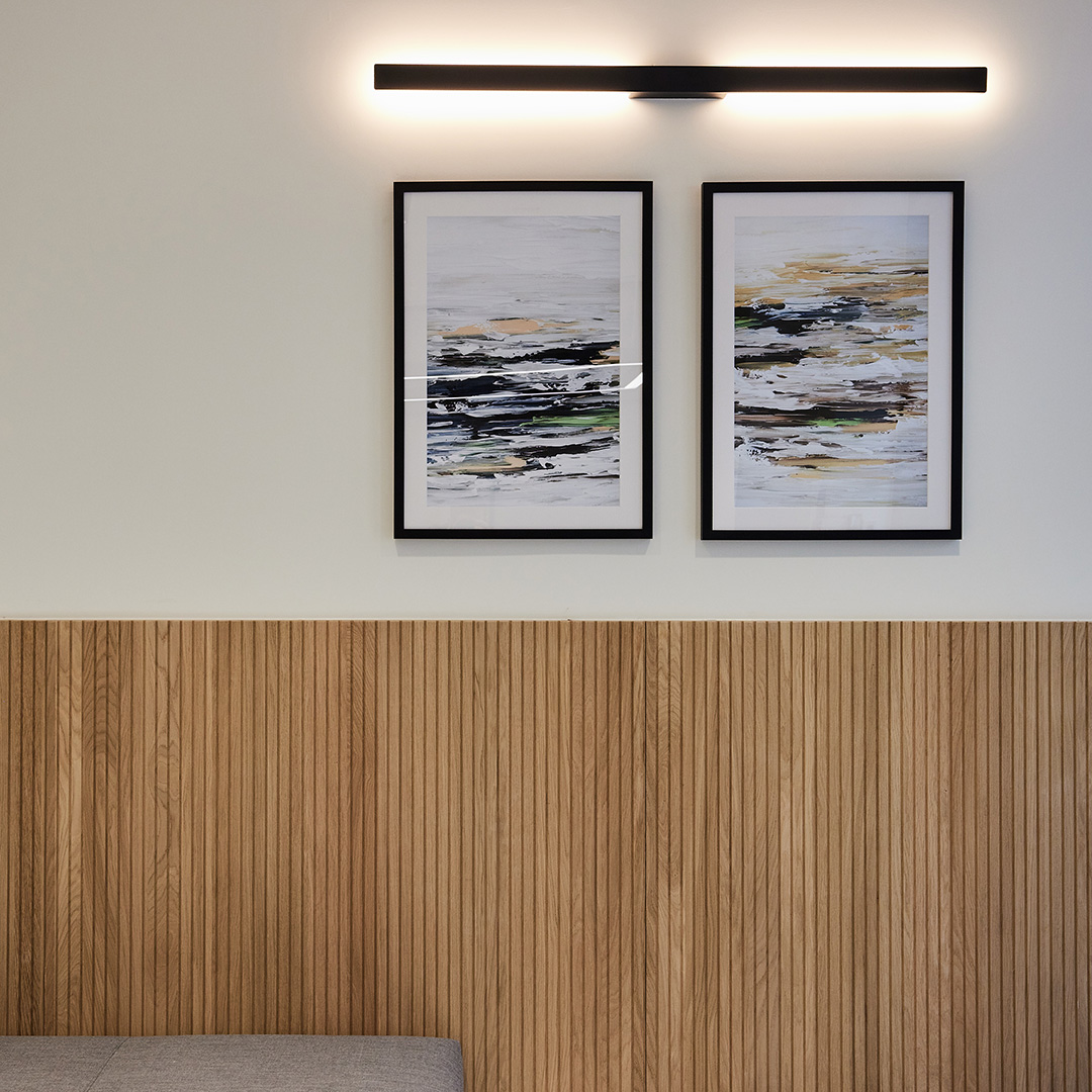 An office reception area, with a half-clad wall in light timber joinery, and two minimalist paintings