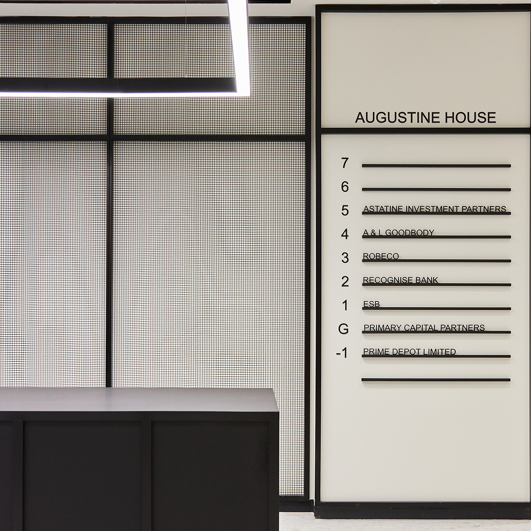 A contemporary office interior design, featuring a black and white reception area, fluorescent pendant lighting and new wayfinding signage