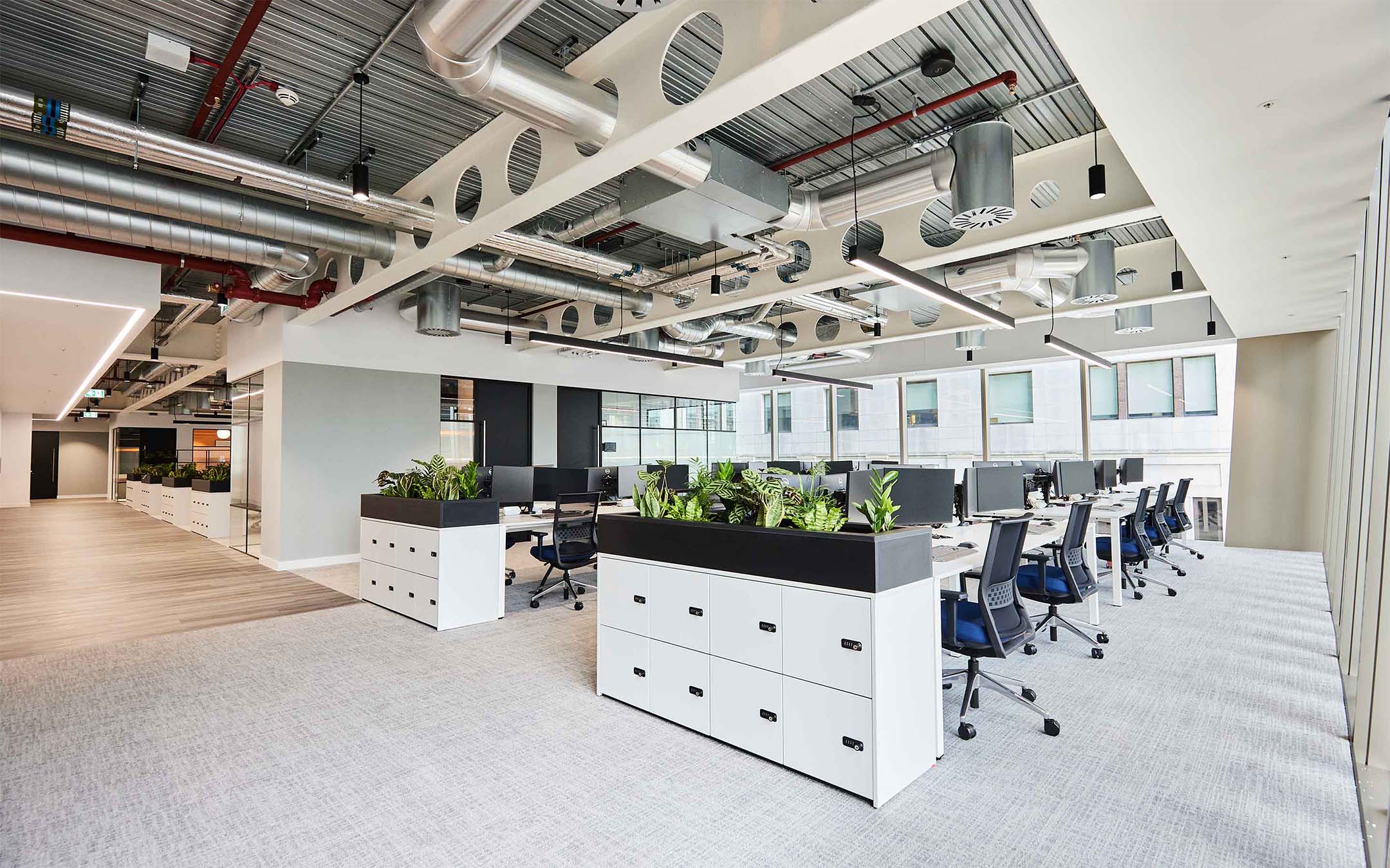 Modern office interior with desks, chairs, and exposed ceiling ducts.