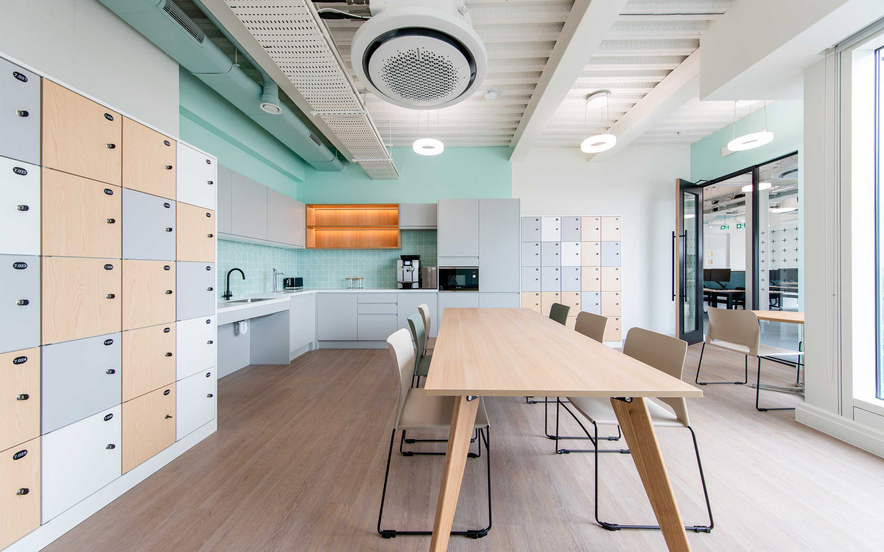 A bright kitchen in a sleek office interior design, with pastel finishes and a large table for socialising