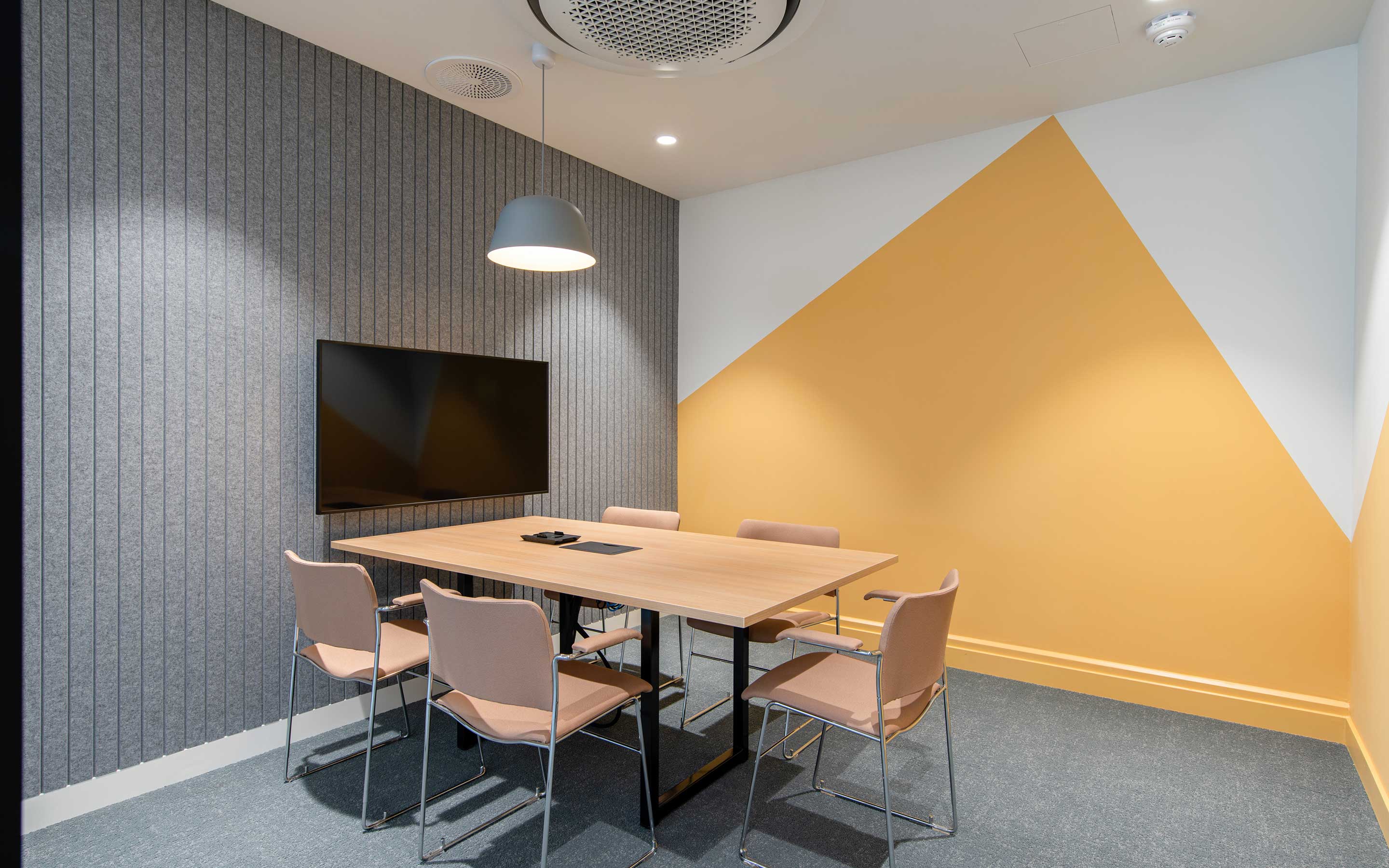 A meeting room in a sleek office interior design, with acoustic panels, sunshine yellow wall detailing, and technology