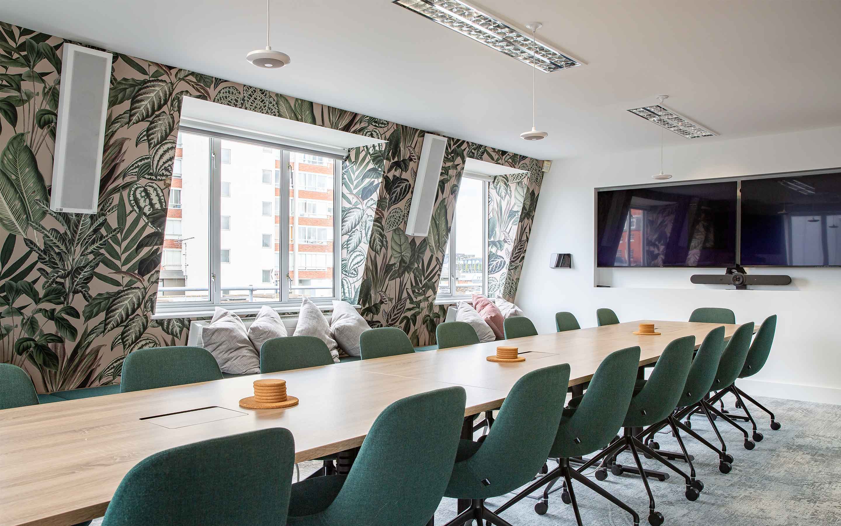 A boardroom within a creative office interior design, complete with floral wallpaper and a large boardroom table with green chairs