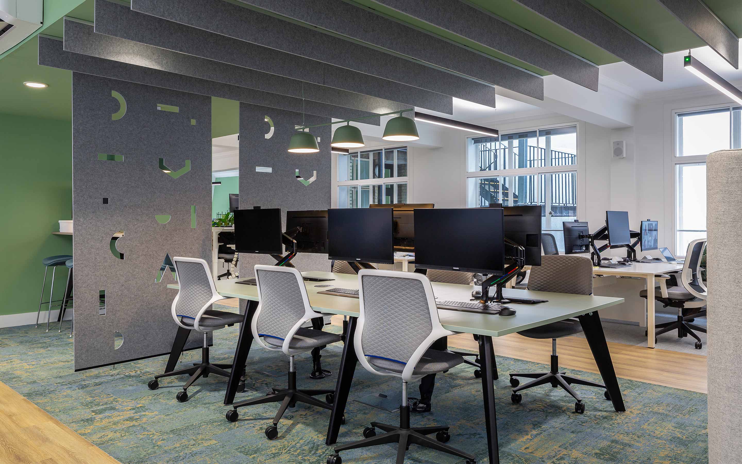 A bank of desks in a creative office interior design, complete with grey fabric acoustic dividers and mint green painted walls