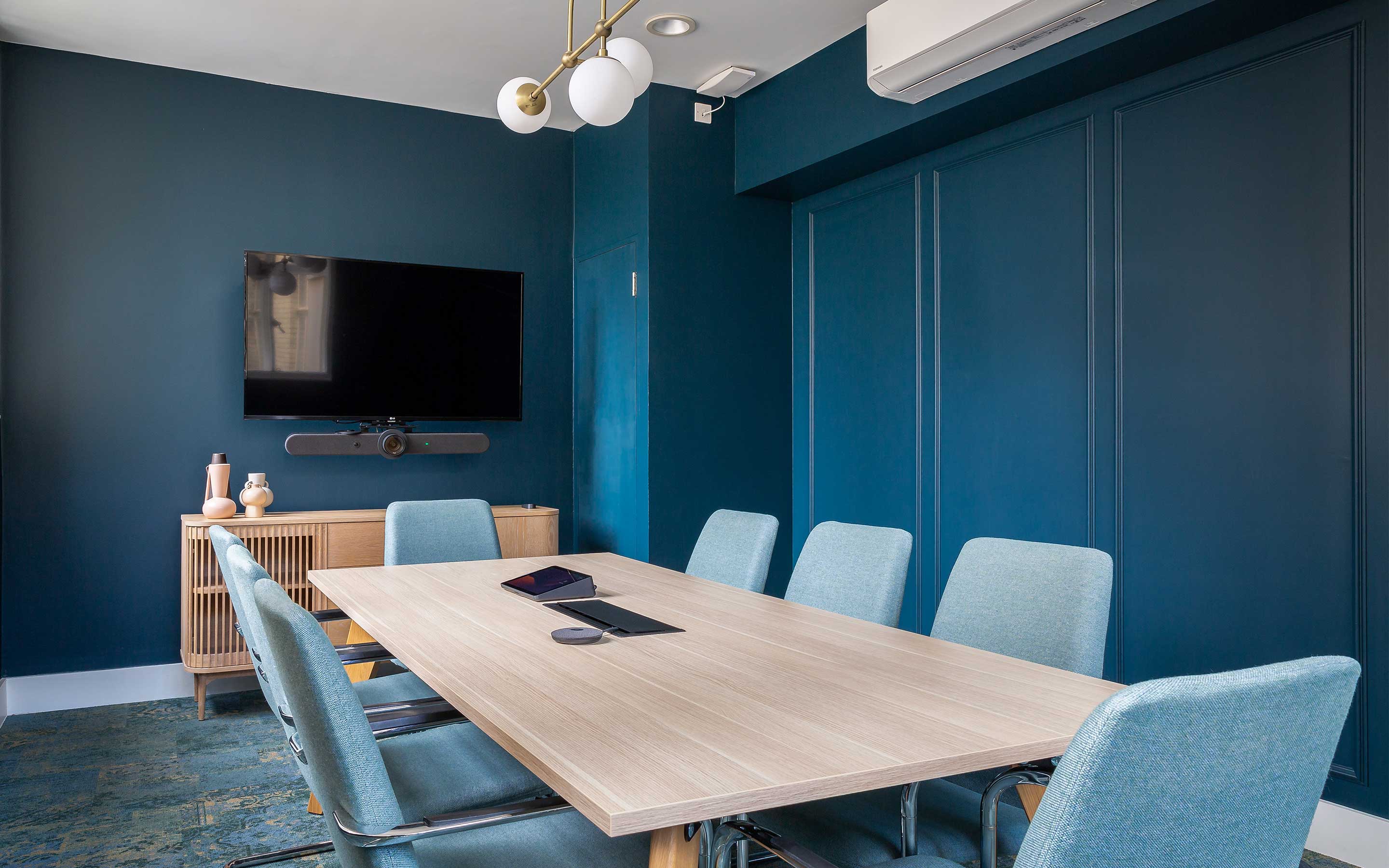 A sleek meeting room with navy walls and a wooden sideboard, in a sophisticated new office interior design