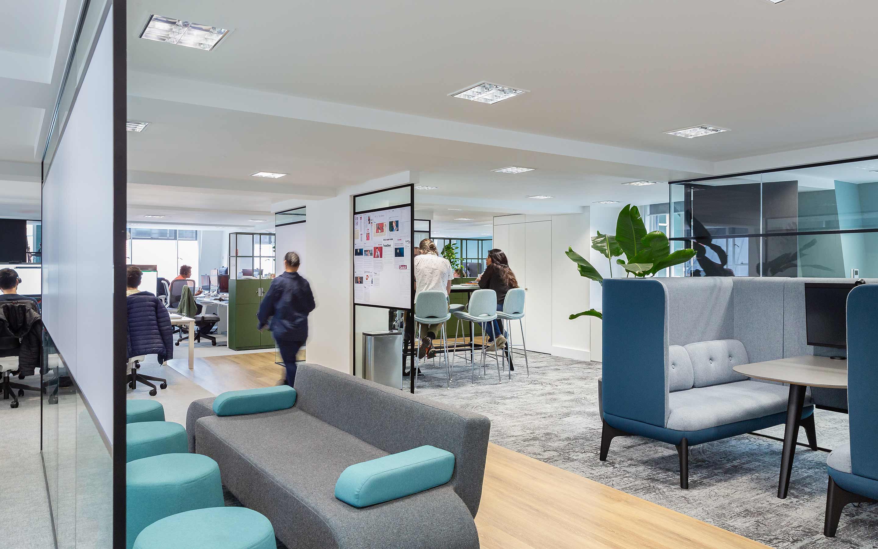 Individuals collaborating in an open plan office in a contemporary workplace, with breakout booths, and a colour palette of blues and greys