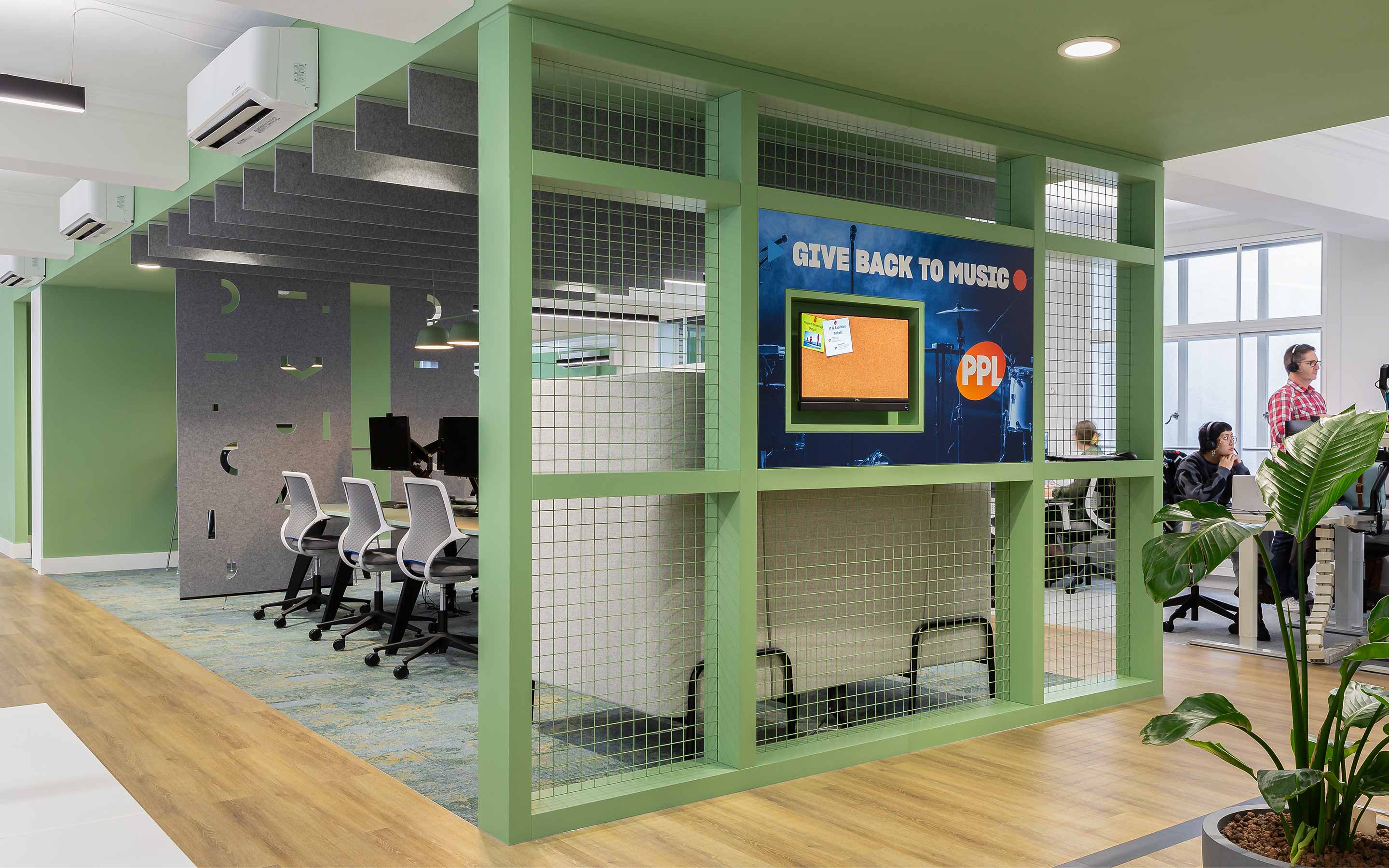 Creative office interior design featuring a collaboration area, musical motifs, pale green painted joinery, and people working in an open plan office