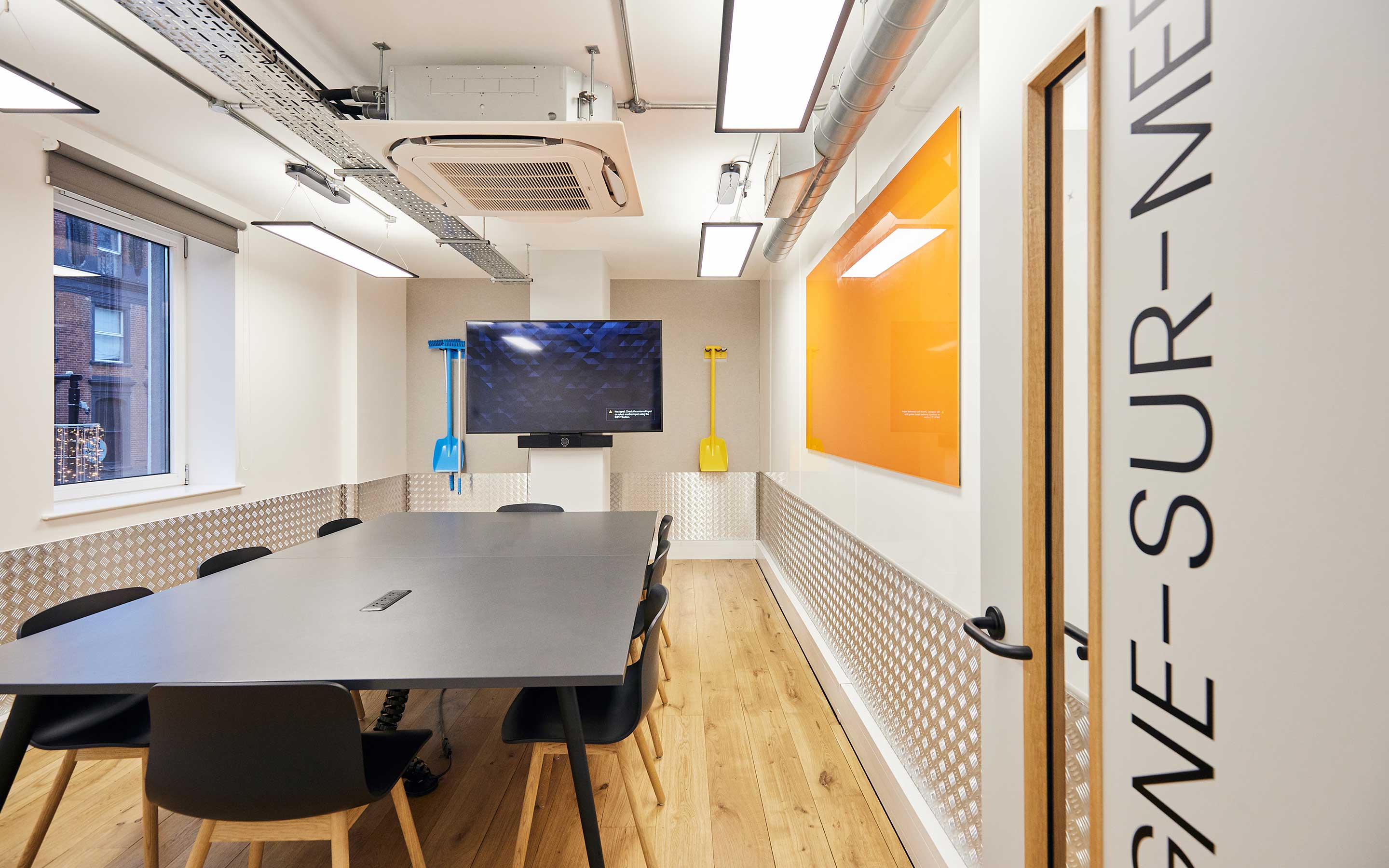A meeting room with tables and chairs and an orange whiteboard in a sleek office interior design