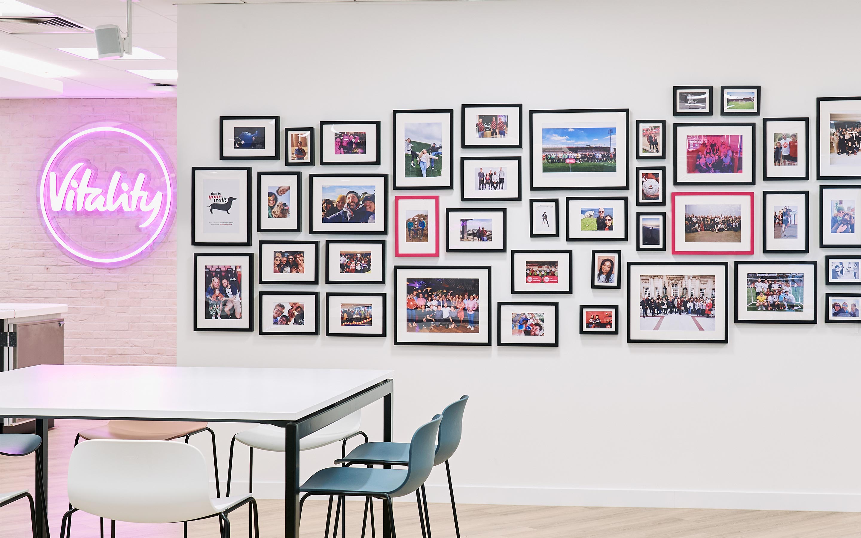 A contemporary office kitchen complete with a culture wall full of photographs and a pink neon logo sign