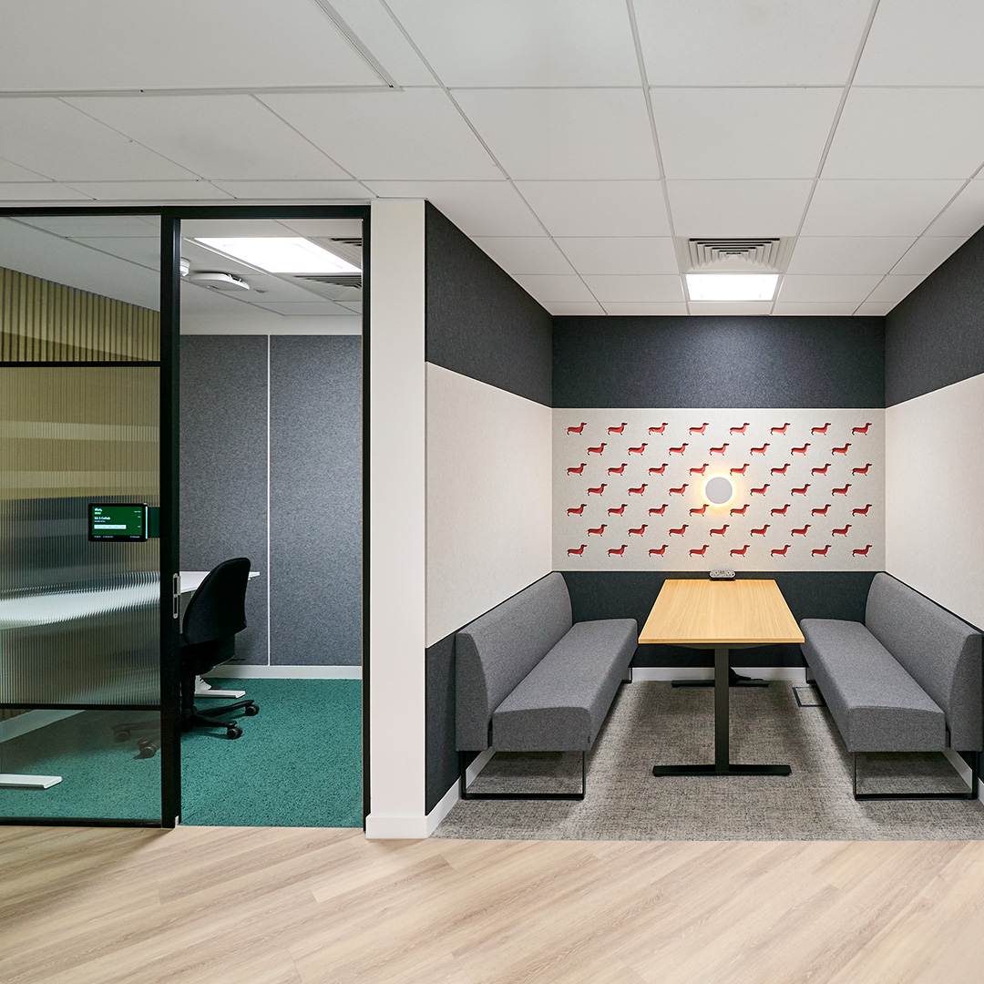 An image of a meeting room and collaborating booth with sleek soft grey seating in a modern office