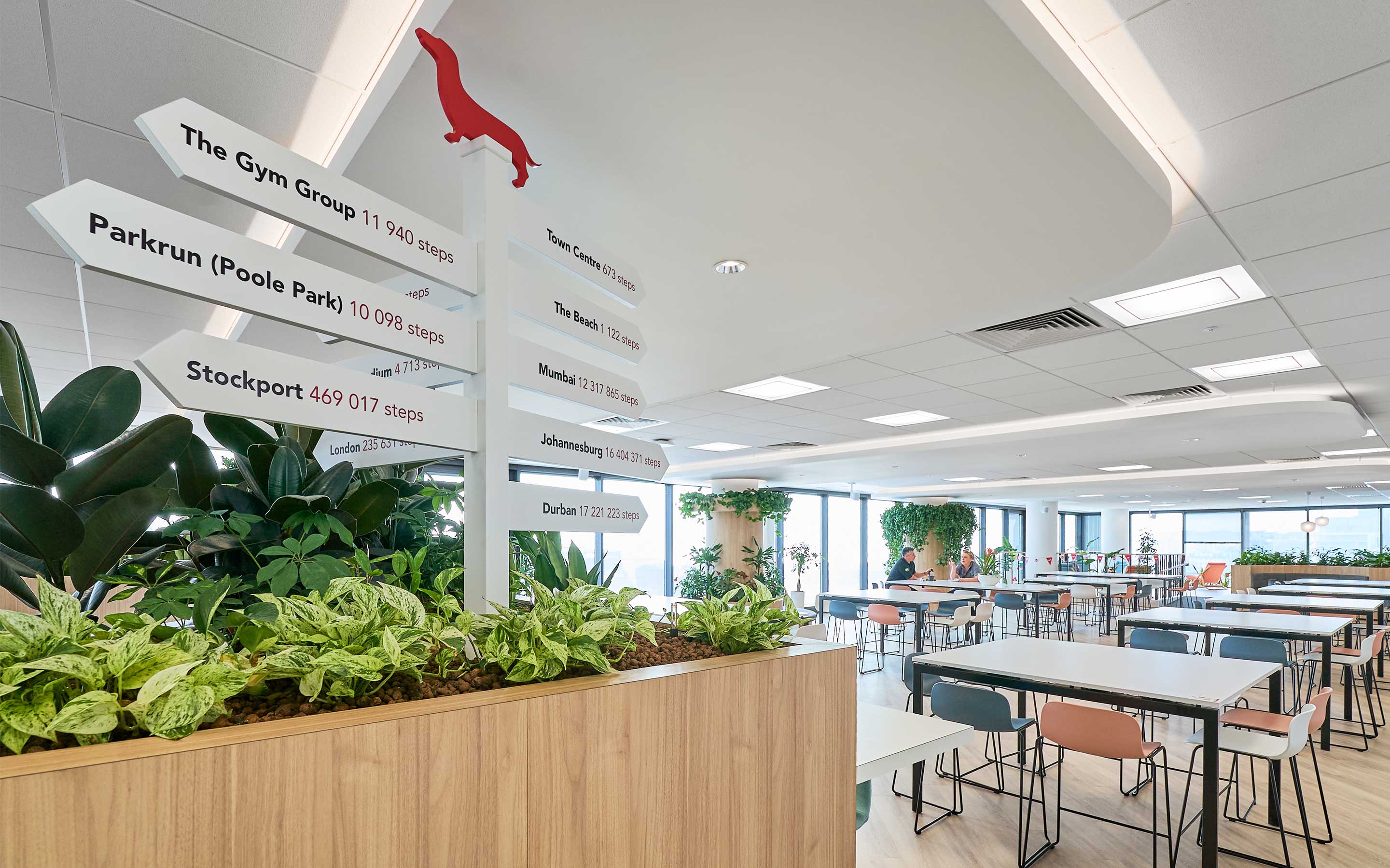 A bright, large canteen in a modern office interior design, with plants and pink and blue chairs