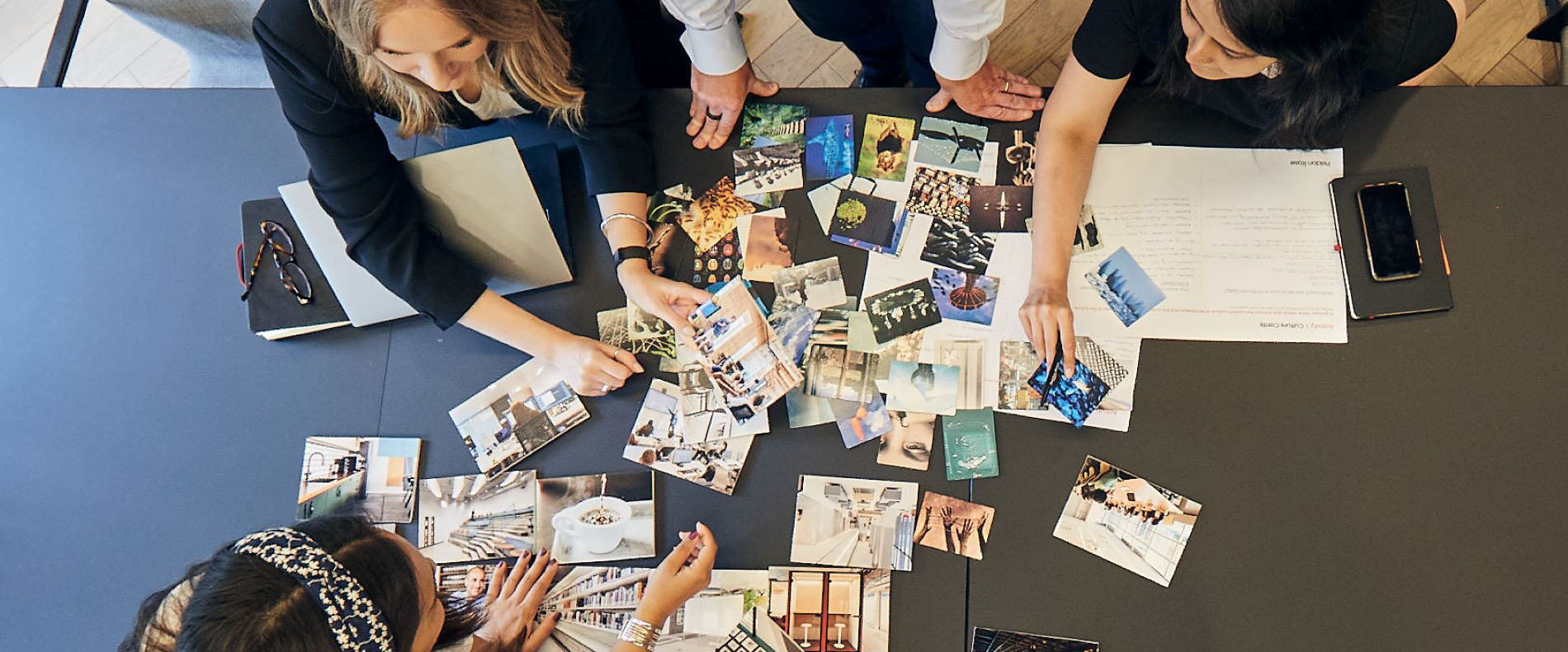 Group of people collaborating over a table with various photos and documents spread out.