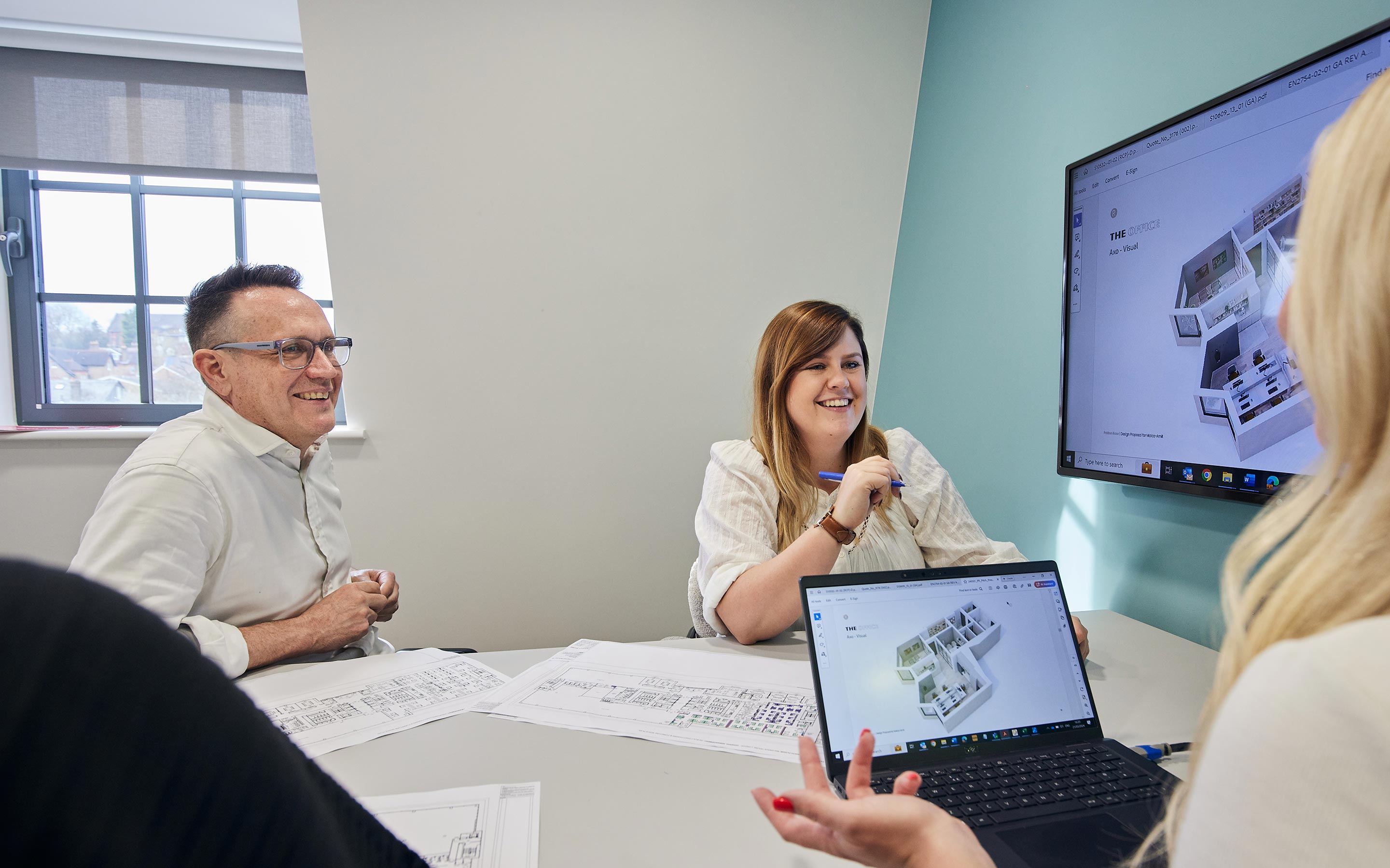 Colleagues collaborating around a table and large computer screen, in a relaxed meeting room