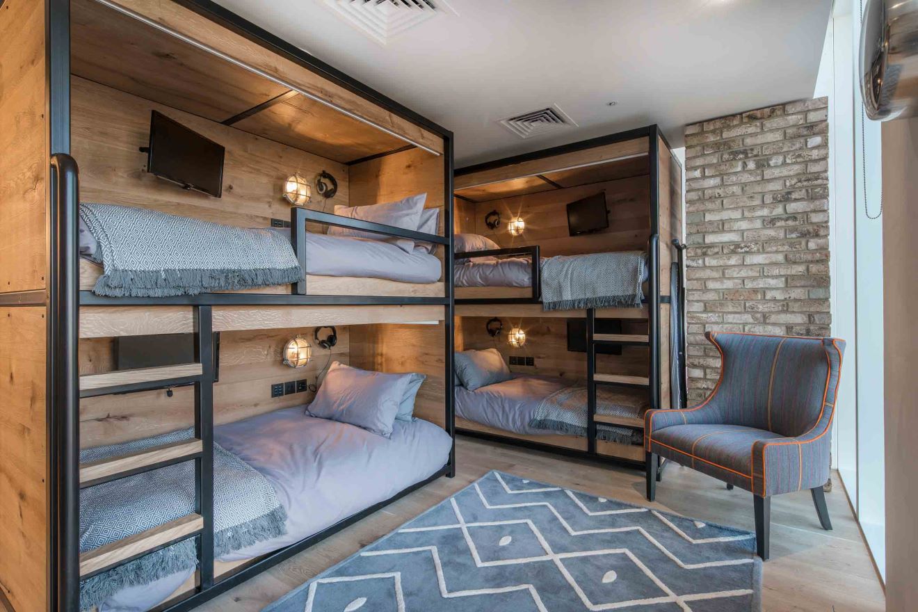 Modern rustic bunk beds in a chic room with wooden panels and stone wall.